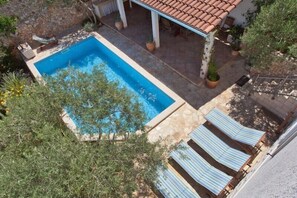 Une piscine rectangulaire, bordée d’une terrasse carrelée, entourée de chaises longues et de plantes en pot.