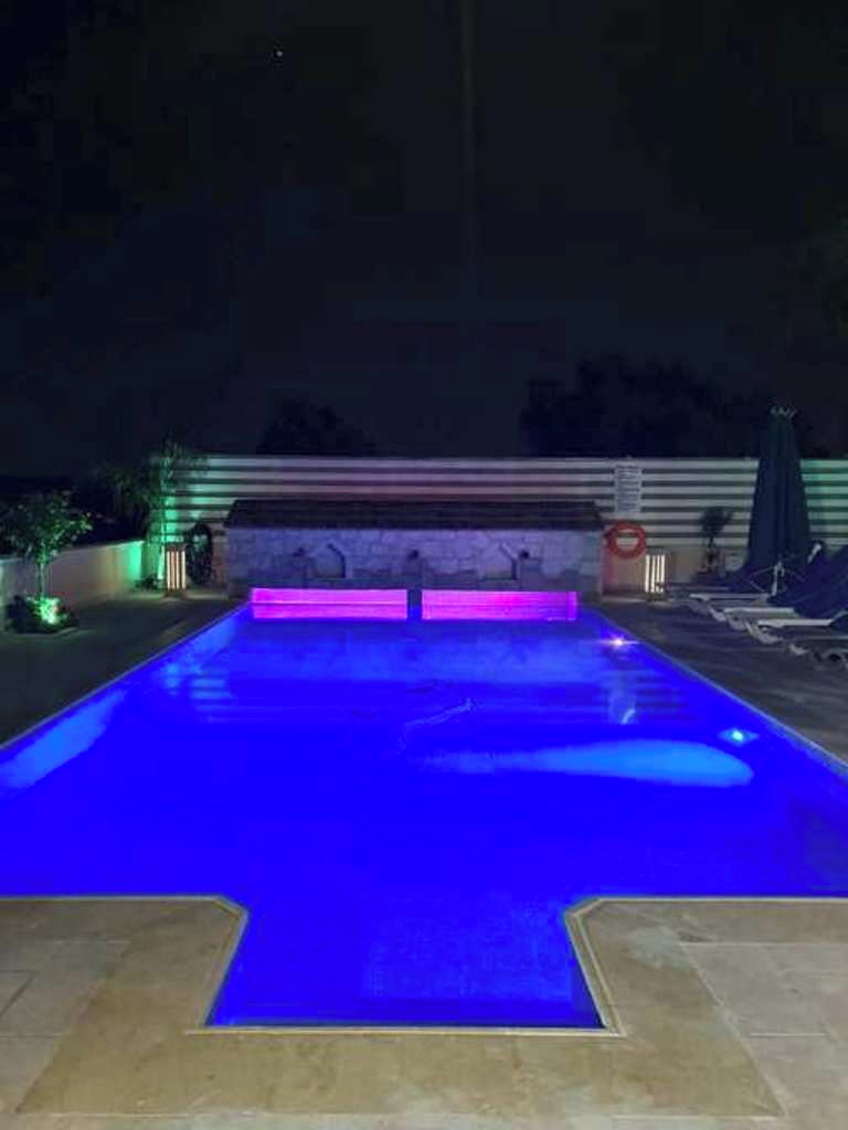 Une piscine dont le bord est illuminé de lumière bleue, entourée d’un petit muret et d’une terrasse carrelée.