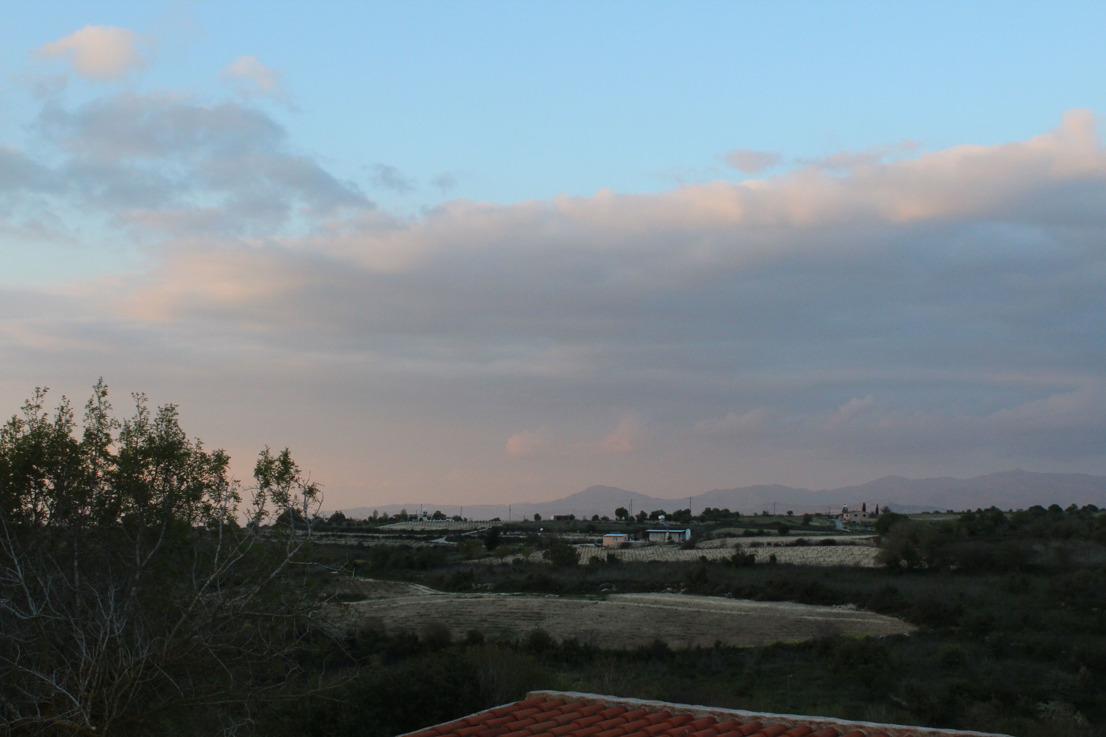 Paisaje rural con cielo despejado, montañas a lo lejos y vegetación escasa.