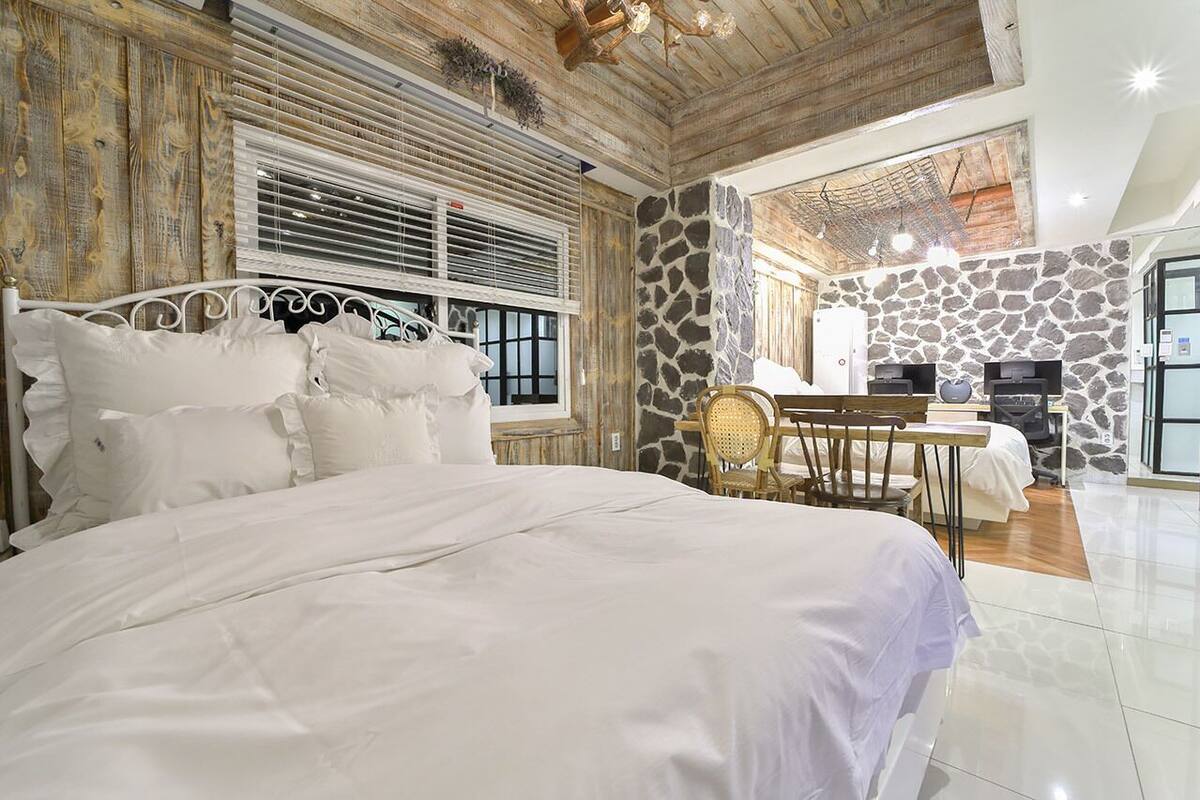 Un dormitorio con una cama grande, paredes de madera, una pared de acento de piedra y una zona de comedor con mesa y sillas.