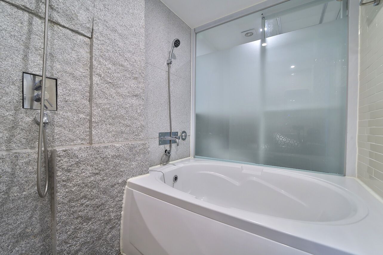 Un baño moderno con una bañera independiente, ducha con mampara de vidrio y pared de piedra texturizada.