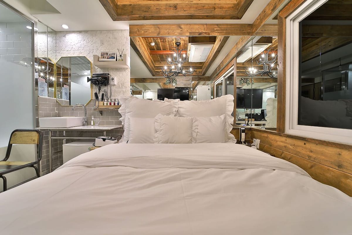 Un dormitorio con una cama grande, techo de madera, un espejo y un baño con lavamanos y espejo.