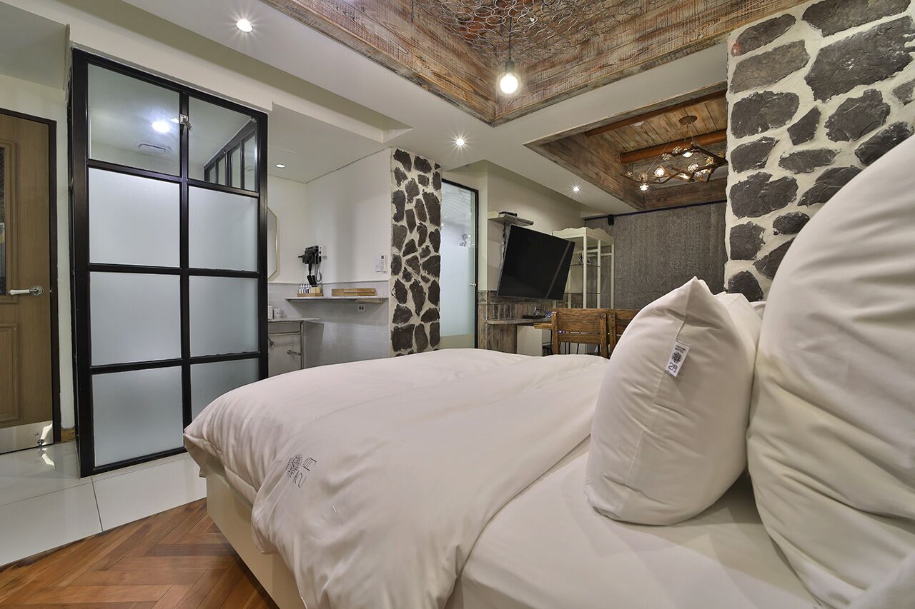Un dormitorio con una cama grande, una pared de acento de piedra, un televisor y un techo de madera.