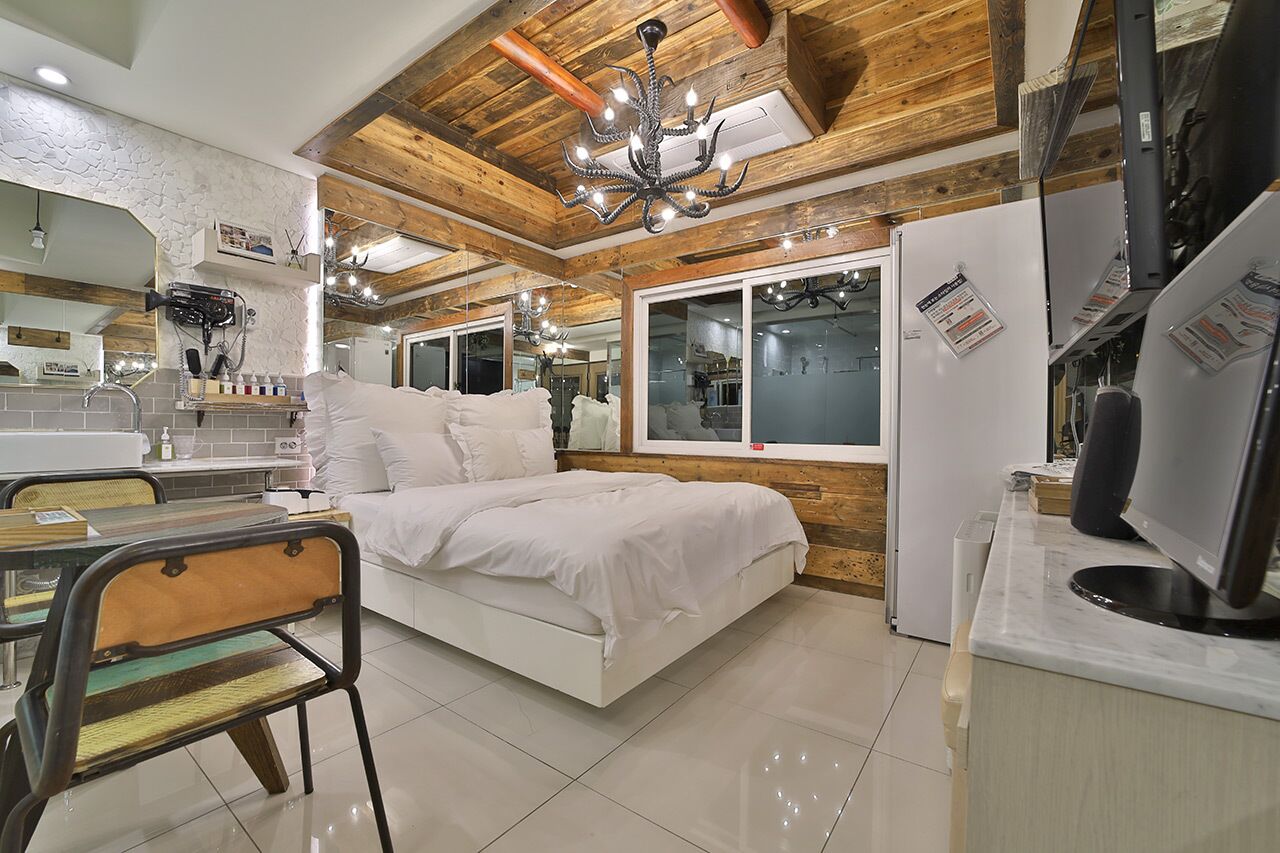 Une chambre moderne avec un lit, un bureau et une chaise. On y trouve également un miroir, un lustre et un réfrigérateur.