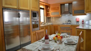 Une cuisine moderne avec des meubles en bois, un réfrigérateur en acier inoxydable, un four et un four à micro-ondes. On y trouve une table à manger mise avec des assiettes, des bols et une bouteille de vin.