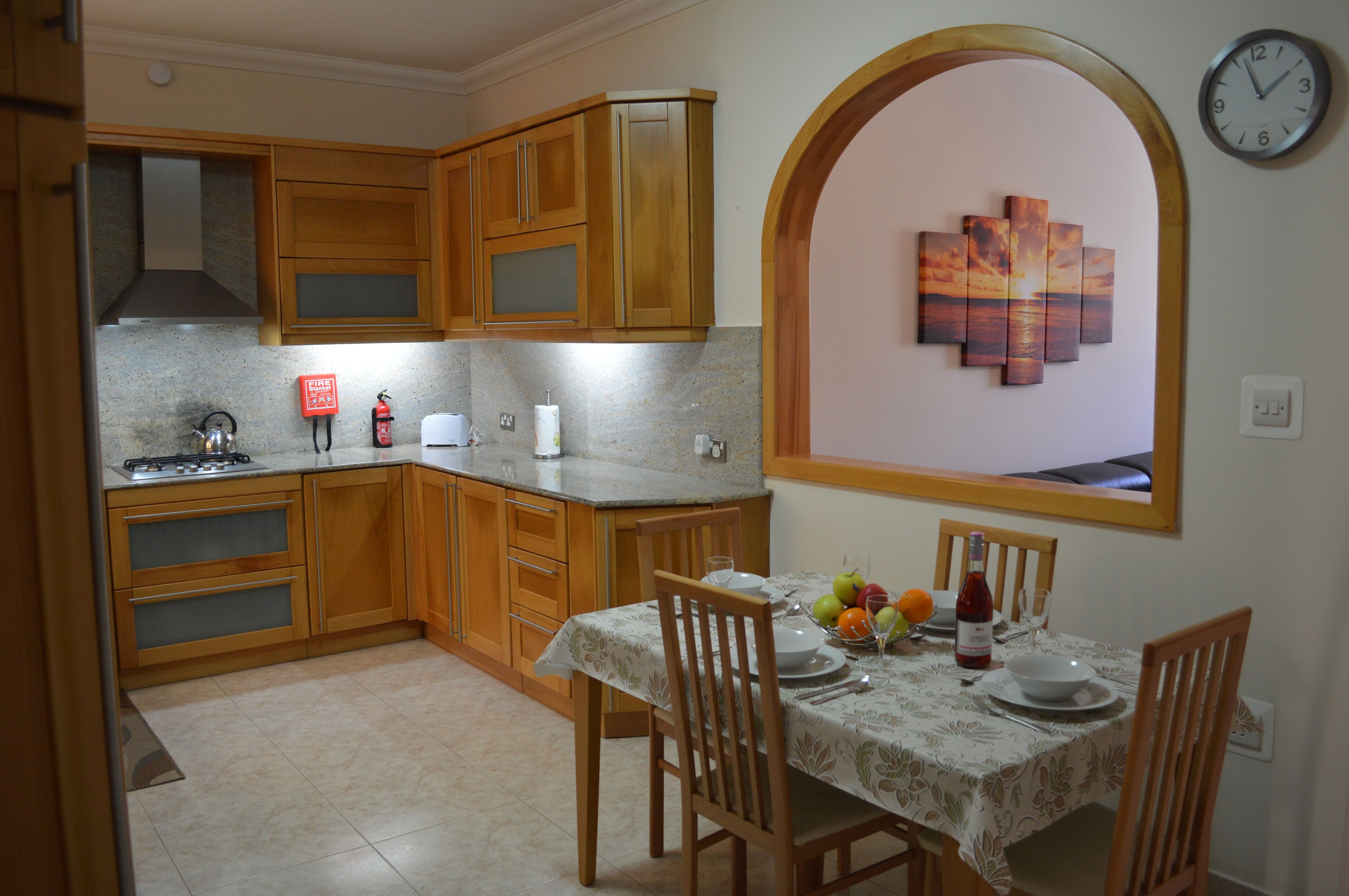 Une cuisine avec des meubles de rangement en bois, une cuisinière à gaz et une table à manger mise pour deux personnes.