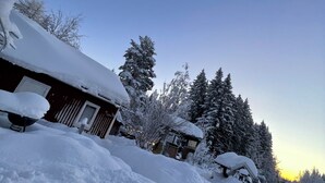A snow-covered landscape with a wooden cabin and snow-laden trees. - Cottage with access to silence, only nature's own sounds. (Åmotsbruk)