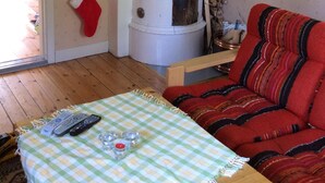 A cozy living room with a checkered tablecloth, a red sofa, a white cylindrical heater, and a painting on the wall. - Cottage with access to silence, only nature's own sounds. (Åmotsbruk)