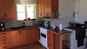 A kitchen with wooden cabinets, a stove, a sink, and a window with curtains. - Cottage with access to silence, only nature's own sounds. (Åmotsbruk)