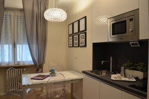 Une cuisine moderne équipée d’un four à micro-ondes encastré, d’un évier et d’un coin repas avec une table et des chaises en verre.