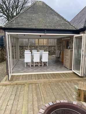 A covered patio with a herringbone floor, a glass enclosure, a stone wall, and a wooden deck.