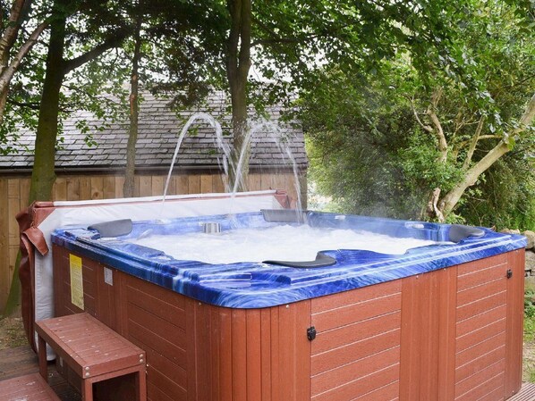 A hot tub with a wooden exterior and a blue interior, surrounded by trees and a wooden fence.