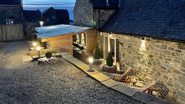 A stone building with a gravel driveway, wooden benches, and outdoor lighting. - 5* Barn Conversion c/w hot tub, sauna, games room, 1/4 acre enclosed games (Stocksfield, Northumberland)