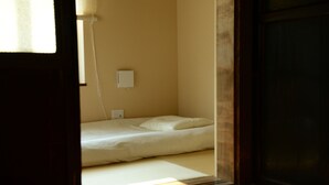A small, dimly lit room with a single bed, a wall socket, and a window with blinds. - Kyoto Guest House Nanni Saiin (Kyoto)