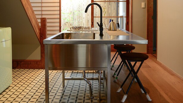 A modern kitchen with a stainless steel island, a black faucet, and a wooden ceiling. - Kyoto Guest House Nanni Saiin (Kyoto)