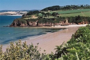 A coastal landscape with a sandy beach, rocky outcrops, and green hills in the background.