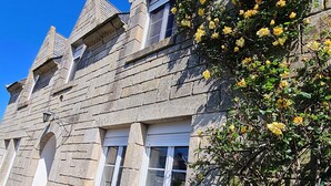 Un edificio in pietra con un tetto spiovente, diverse finestre e un cespuglio fiorito.