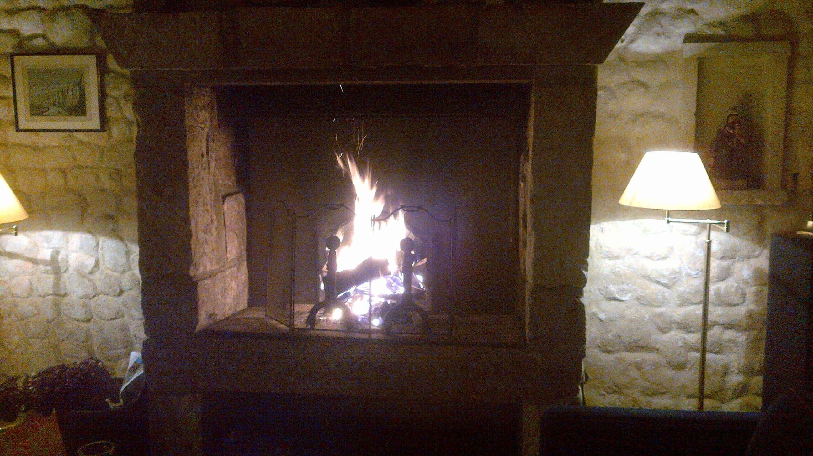 Une cheminée en pierre avec un feu, flanquée de deux lampes.