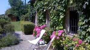 A garden area with a paved path, two white lounge chairs, and pink flowering plants. - Charming House, Edge of the Golf, Sea, Countryside, Peaceful (Seine-Maritime)