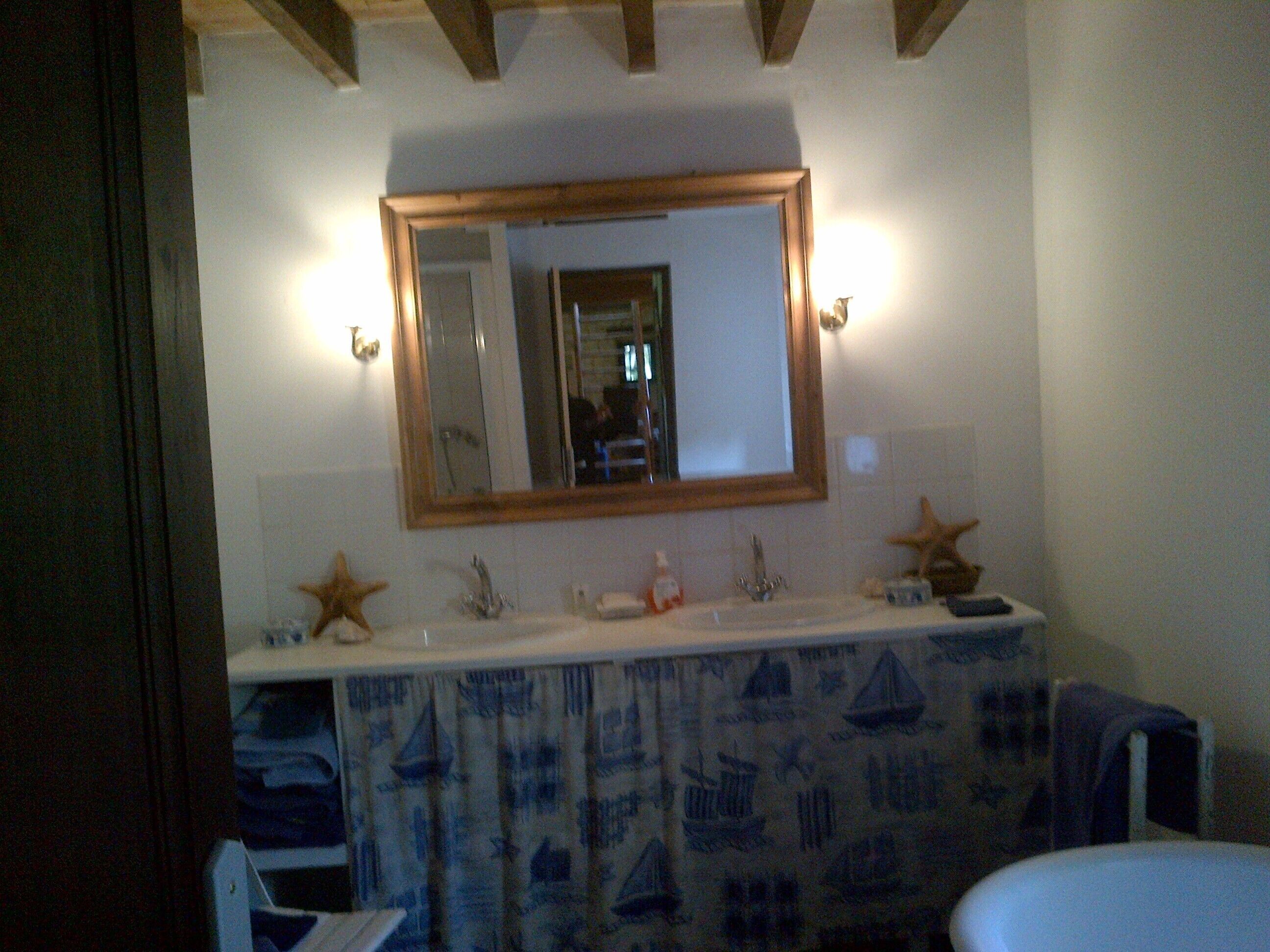 A bathroom with a wooden ceiling, a large mirror, a sink with two starfish decorations, and a patterned curtain.