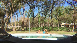 Una persona sdraiata su un solarium con vista su una piscina e alberi.