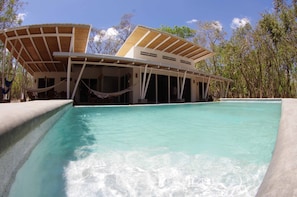 A modern pool area with a clear blue pool, a covered seating area, and a view of the surrounding trees.
