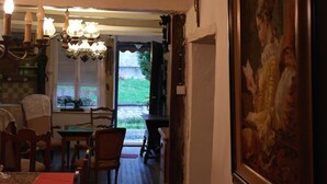 A dining area with a red tablecloth, wooden chairs, a chandelier, and a painting on the wall.