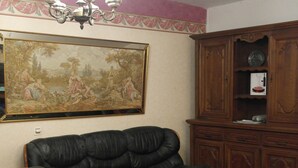 A living room with a black leather sofa, a wooden coffee table, and a large classical-style painting on the wall.