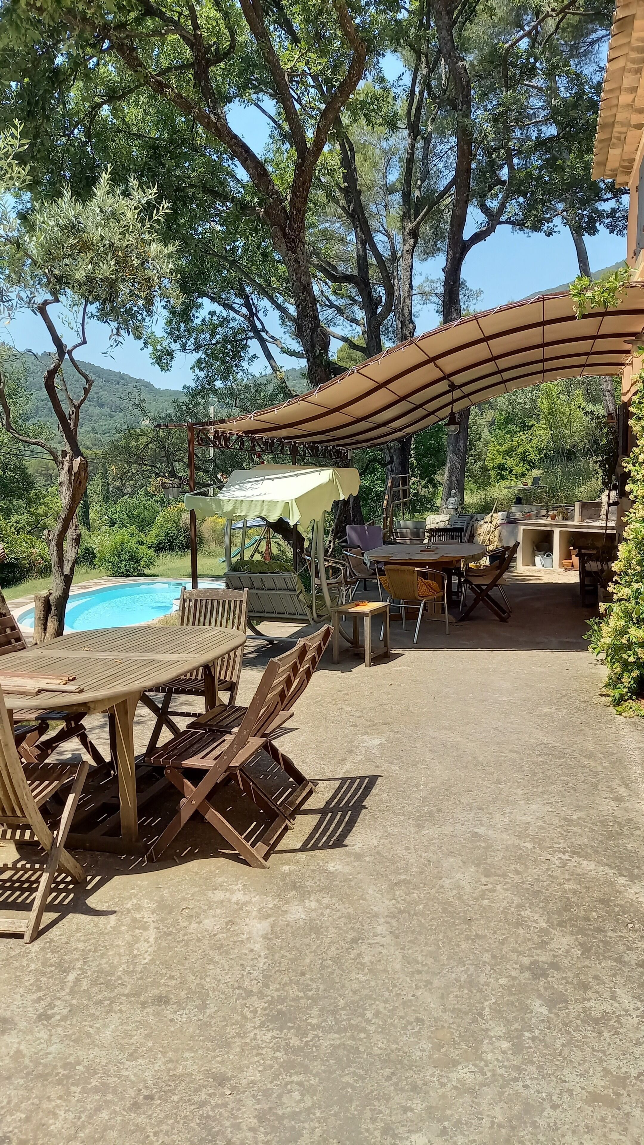 Una zona patio esterna con piscina, mobili in legno e un'area salotto coperta.