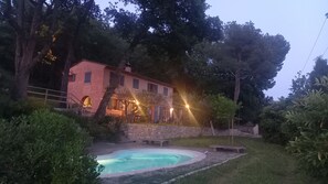 A pink villa with a swimming pool, surrounded by trees and stone walls.