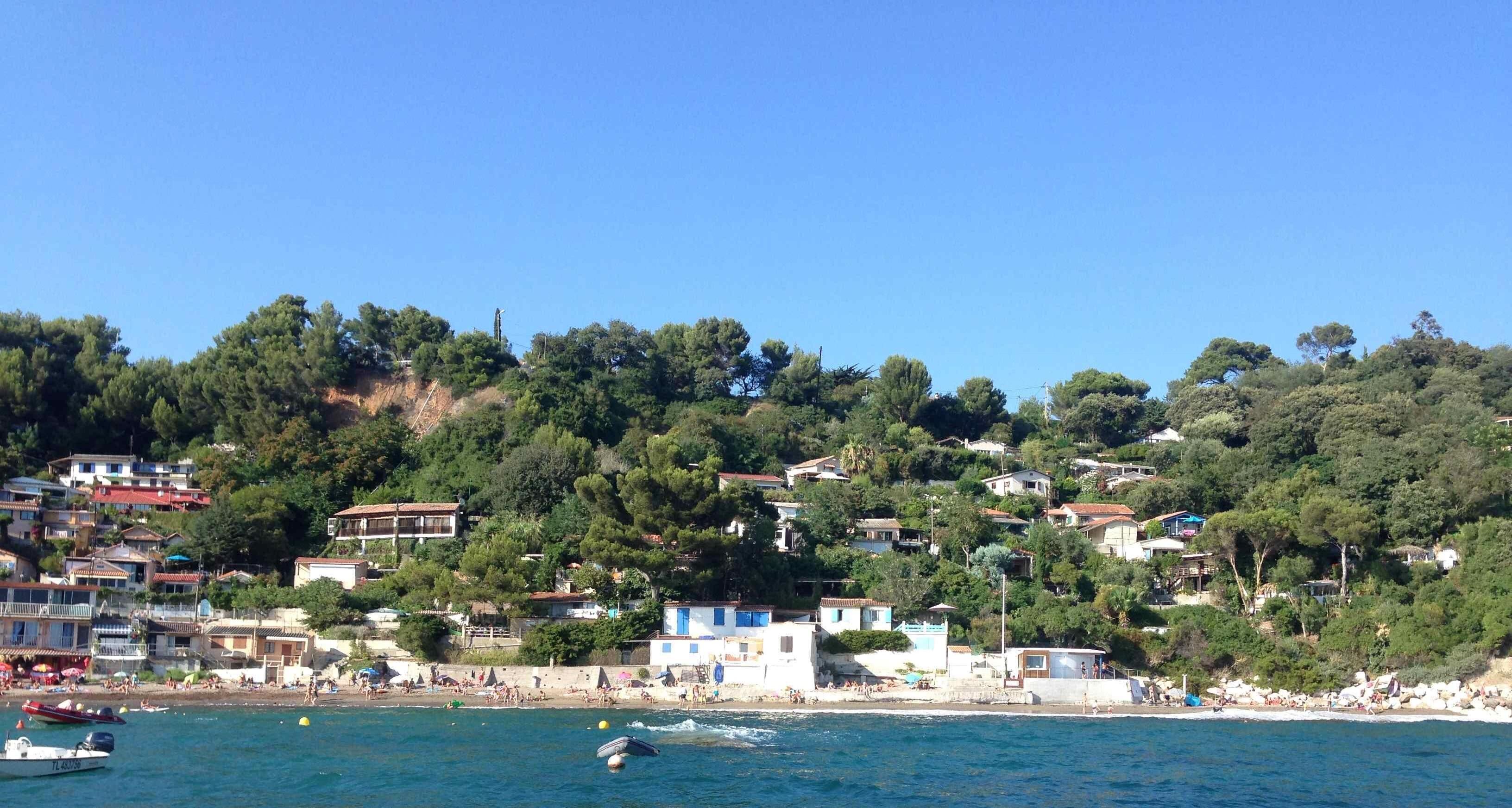 Une ville côtière avec des maisons construites sur une colline, une plage animée et des bateaux sur l’eau.