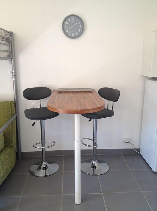 A small kitchen with a wooden table and two bar stools. A clock is mounted on the wall above the table. - Le Pradet - Studio 4 pers à 10min à pied de la Plage - Roses (Le Pradet)