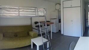 Ett litet rum med en våningssäng, en soffa, ett litet bord, ett skåp och en mikrovågsugn.