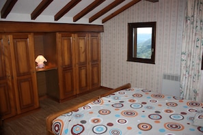A bedroom with a bed, wooden wardrobe, and a window with a view.