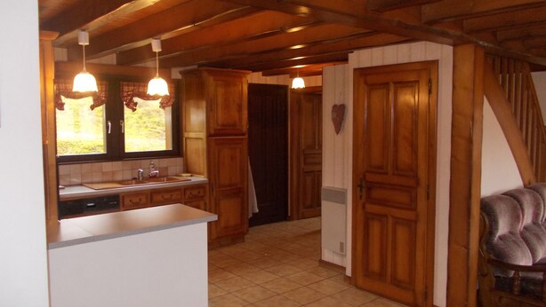 Een keuken met houten kastjes, een wit aanrechtblad en een raam met gordijnen.