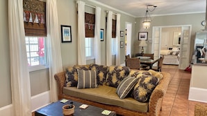 A living room with a sofa, a dining table, and chairs. There is a kitchen area in the background.