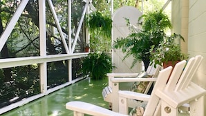 A covered outdoor seating area with white chairs and tables, surrounded by greenery and potted plants.