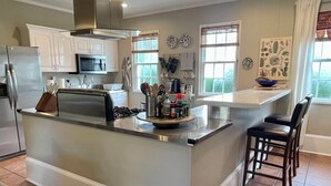 A modern kitchen with stainless steel appliances, a central island, and a dining area with a view of the outdoors.