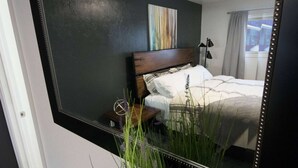 Une chambre d’hôtel avec un grand miroir, un lit avec une literie blanche, une petite table de chevet et une plante en pot.