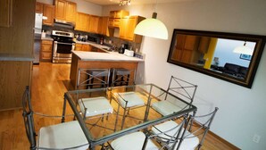 Une cuisine moderne avec des meubles en bois, des appareils en acier inoxydable et un coin repas comprenant des chaises en métal et une table en verre.
