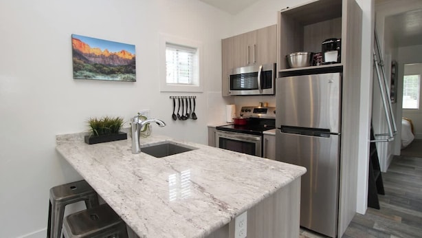 A modern kitchen with a marble countertop, stainless steel appliances, and a window with blinds. - Tiny Home near Zion with Loft & Resort Pools (Orderville)