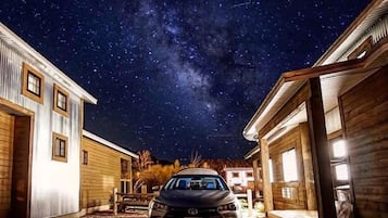 A residential area at night with a car parked in front of a house, under a starry sky.
