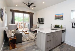 A modern kitchen with a central island, a dining area with a table and chairs, and a large window with curtains. - Tiny Home near Zion with Loft & Resort Pools (Orderville)