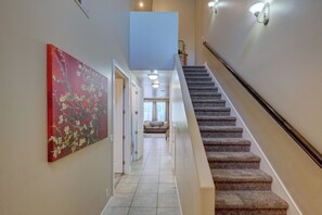 A hallway with a carpeted staircase, a red floral painting on the wall, and a view into a living area with a sofa and a window. -  St George, near Zion 2 king beds, 2 pools/hot tubs, fish pond  (Washington)