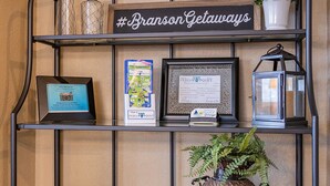 Ein Metallregal mit einem Schild mit der Aufschrift "#BransonGetaways", einem gerahmten Zertifikat, einer Karte, einer Laterne, einer Schüssel, einer Topfpflanze und einer Zeitschrift auf einem Tisch.
