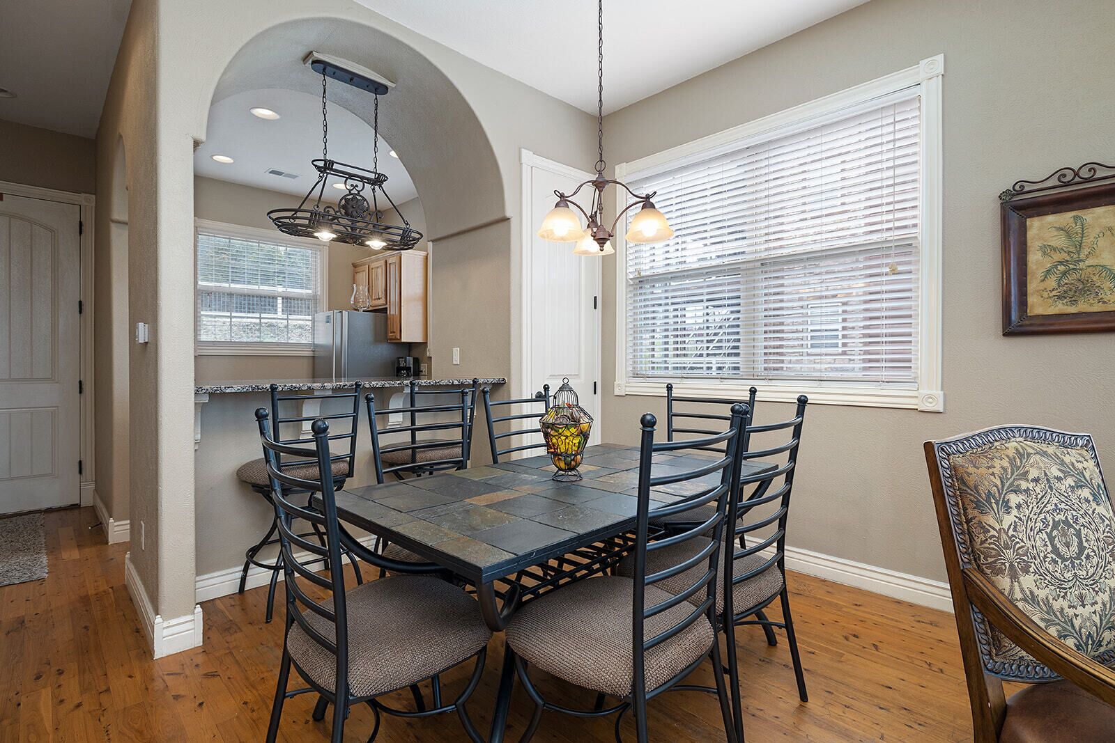 A dining area with a dark wooden table and chairs, a chandelier, and a window with blinds.