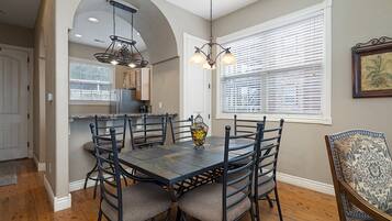 A dining area with a dark wooden table and chairs, a chandelier, and a window with blinds.