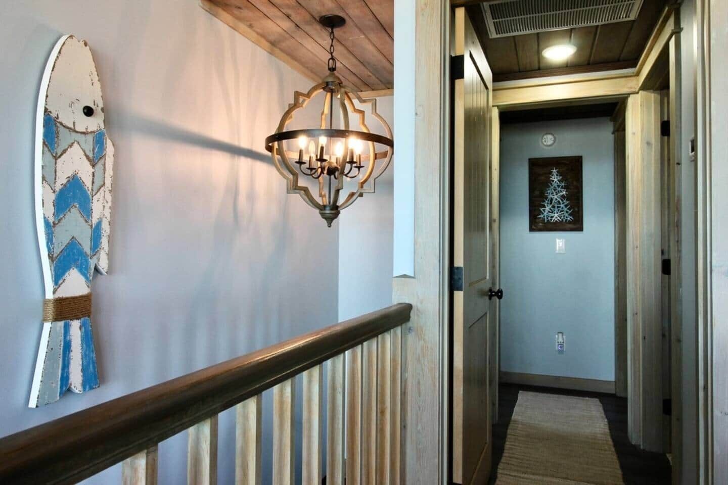 Ein Korridor mit Holzbalkon, einem Kronleuchter und einer Surfbrett-Dekoration an der Wand.