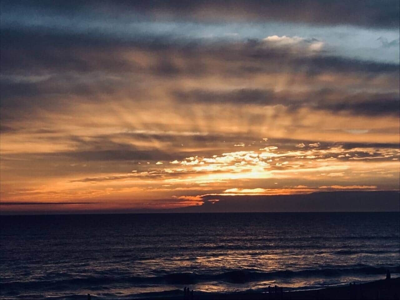 Un atardecer sobre el océano con la silueta de una persona al frente.
