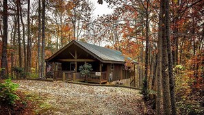 A rustic cabin with a porch, surrounded by autumn foliage.